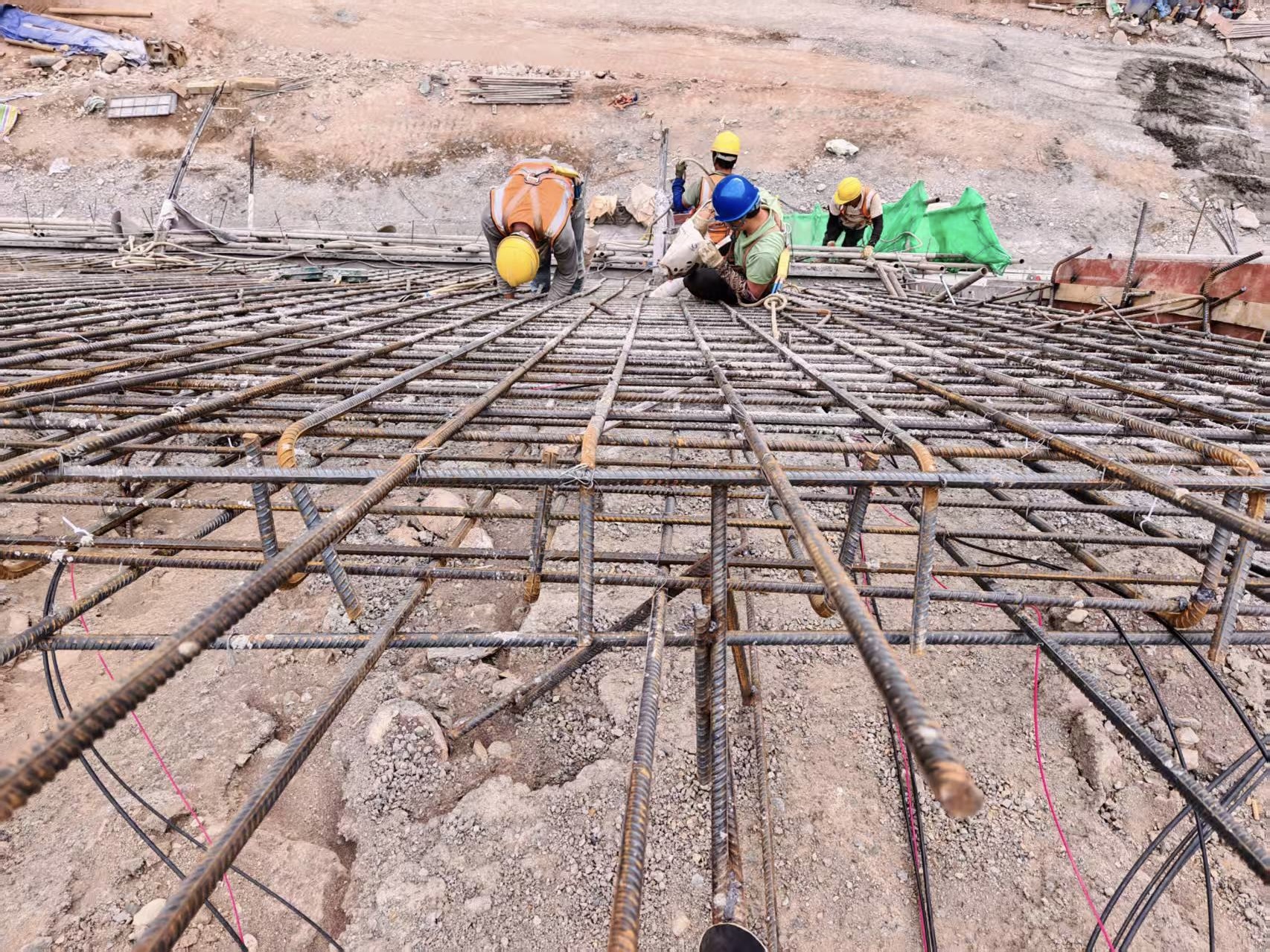 Workers on the reinforcement grid with cable runs visible before concrete placement