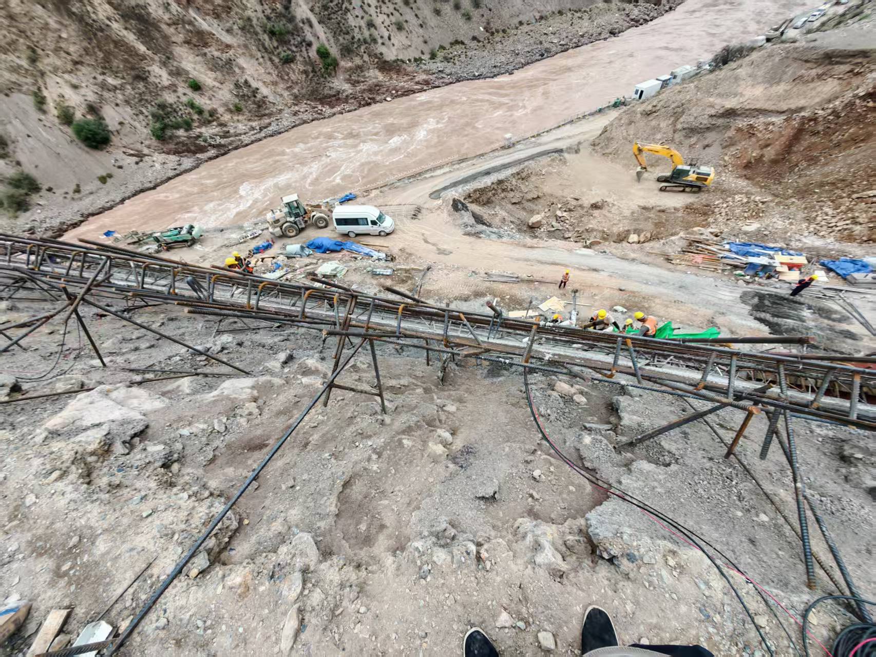 View down the reinforced slope toward the river valley and active construction area